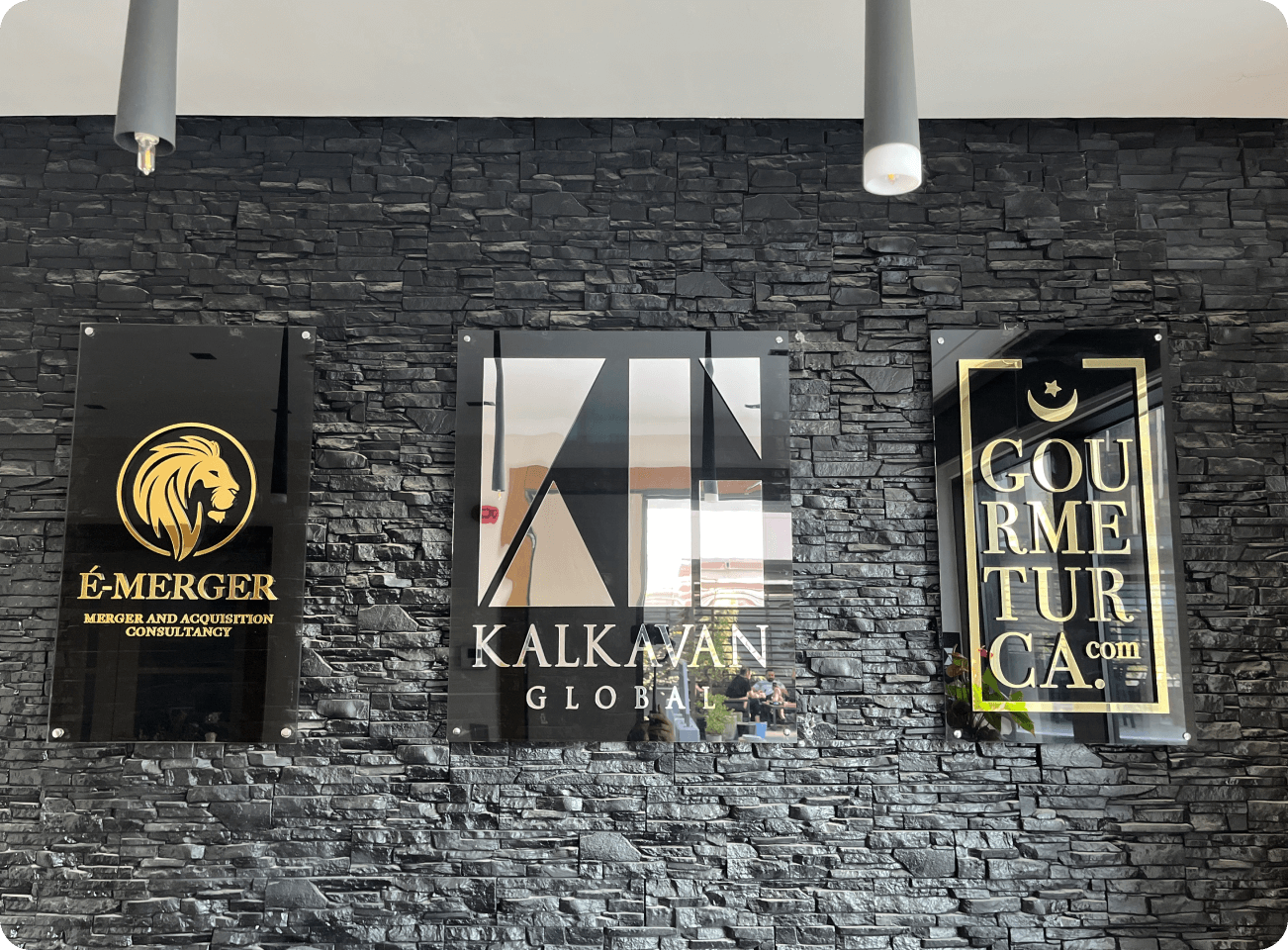 E-merger, kalkavan global and gourmeturca logo on a black concrete wall with lighting